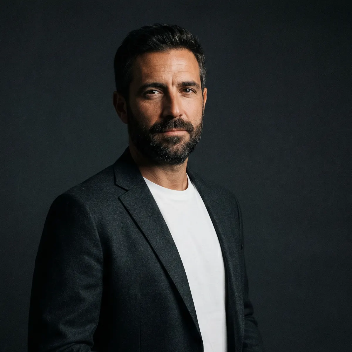 Hombre mediterráneo de unos 40 años con blazer anthracita, retrato editorial en tonos oscuros